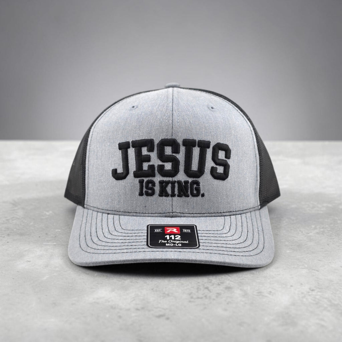 Jesus Is King Christian hat, 3D puff embroidered Richardson 112 trucker hat - straight-on view of raised black lettering and grey brim